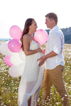 Portrait of a family in the chamomile field. Pregnant woman holds beads. Family with balloons.の写真素材
