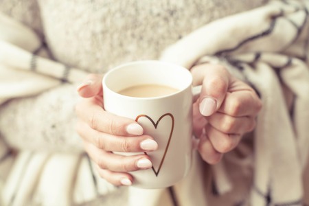 Women's hands hold a hot mug of coffee. Young woman ukutannaja in plaid keeps a cup of cocoa. Holidays. Cozy autumn.の写真素材