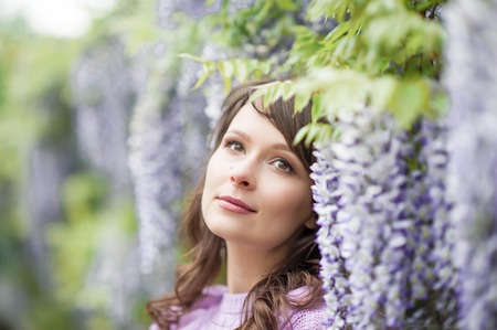 Portrait of a beautiful young brunette woman. A young woman is walking along the spring park. The girl is standing near the wisteria. Blooming park. Spring. Beauty.の写真素材