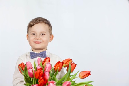 Cute little boy holding a bouquet of flowers. Tulips. Mothers Day. International Womens Day. Portrait of a happy little boy onの写真素材