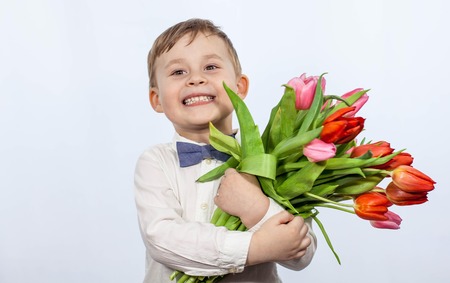 Cute little boy holding a bouquet of flowers. Tulips. Mothers Day. International Women's Day. Portrait of a happy little boy on a white background. Spring.の写真素材