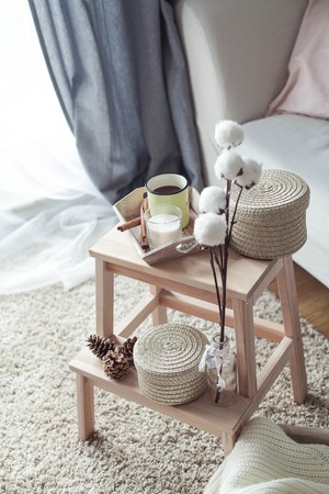 Home decor. A wooden bedside table, a sofa, a cotton, a mug of hot coffee, a knitted plaid. Warm house. Autumn. Cozy. House. The book and glasses. Interior. Springの写真素材