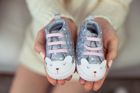 A pregnant woman in a knitted dress sits on the sofa and holds children's shoes.の写真素材