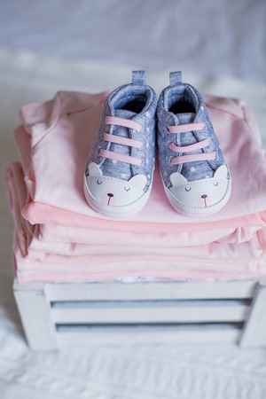 Children's shoes and clothes on the bed. Beautiful pink baby clothes. Newborn. Home cosiness.の写真素材