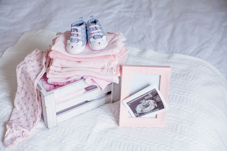 Children's shoes and clothes on the bed. Beautiful pink baby clothes. Newborn. Home cosiness.の写真素材