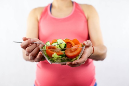 Young beautiful pregnant woman is eating vegetable salad. The girl is holding a plate of salad. Healthy eating. Pregnancy. Motherhood.の写真素材