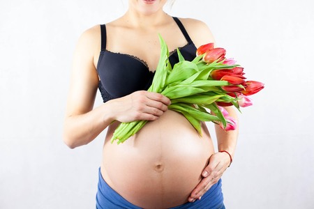 A young beautiful pregnant woman is holding a bouquet of tulips. Portrait of a pregnant woman on a white background. Pregnancy. Motherhood. Love.の写真素材