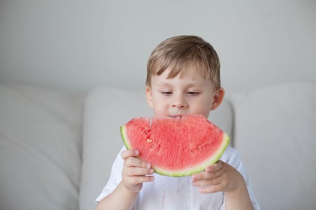 A small cute boy 4 years old is eating a watermelon. Summer. Heat. Watermelon. Portrait of a happy boy with a watermelon. Bright hues.の写真素材