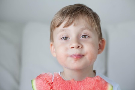 A small cute boy 4 years old is eating a watermelon. Summer. Heat. Watermelon. Portrait of a happy boy with a watermelon. Bright hues.の写真素材