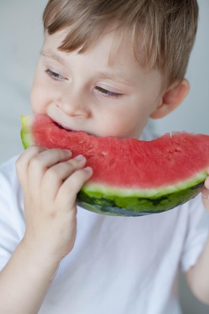 A small cute boy 4 years old is eating a watermelon. Summer. Heat. Watermelon. Portrait of a happy boy with a watermelon. Bright hues.の写真素材