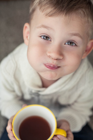 A cozy autumn portrait of a nice little boy. A small boy of 4 years old sits on a carpet and drinks cocoa. Autumn.の写真素材