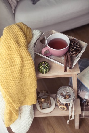 Knitted, warm sweaters, a cup of hot tea, autumn decor, a book, a pumpkin on a wooden chair. Cozy, autumn decor. Autumn interior, sofa. Fall. Winter.の写真素材
