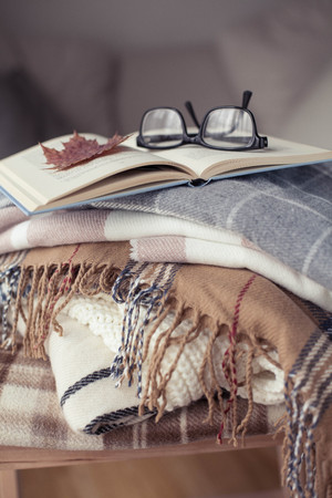 Plaids. Autumn cozy interior. On a wooden chair is a stack of warm blankets. Book and glasses. Autumn. Winter.の写真素材