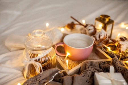 Mug of hot cappuccino on a wooden tray is on the bed. Cozy decor. Breakfast. Mug, plaid, cotton,...
