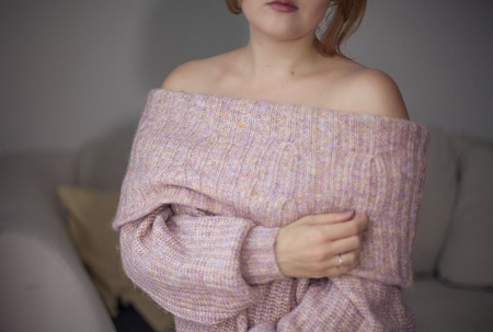 Close-up. Female hands holding a large pink mug of tea. The girl in the knitted sweater drinks...