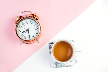 An alarm clock and a cup of tea on a pink white background. Spring.