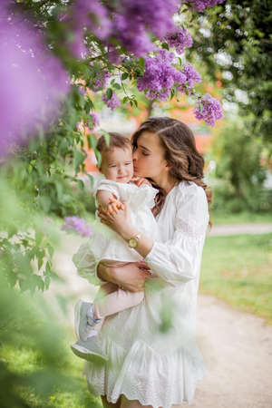 Beautiful young mother and little cute daughter are happy near the lilac. Portrait of mom and daughter.の写真素材