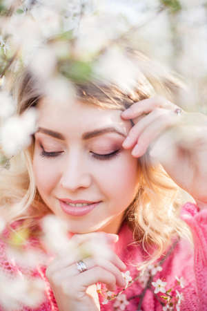 Spring portrait of a young blonde near a flowering tree. Happy young woman. Spring.