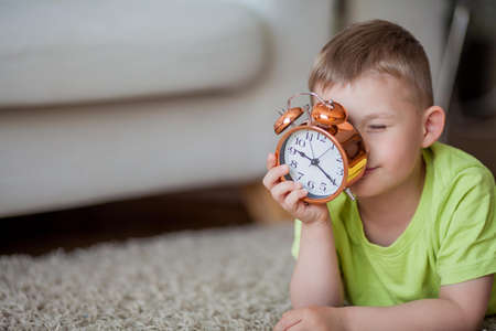 Cute little boy of 4 years old lies on the carpet and near the alarm clock. Morning. Awakening....