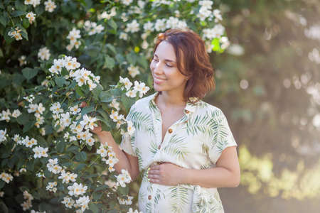 Beautiful young happy pregnant woman is standing near the blossoming tree. Motherhood. Love.の写真素材