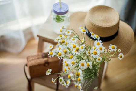 Little wicker women bag, a bouquet of daisies, lemonade with mint, wicker hat, wooden chair. Cozy.の写真素材