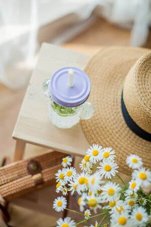 Little wicker women bag, a bouquet of daisies, lemonade with mint, wicker hat, wooden chair. Cozy.の写真素材