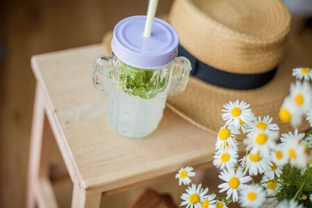 Little wicker women bag, a bouquet of daisies, lemonade with mint, wicker hat, wooden chair. Cozy.の写真素材