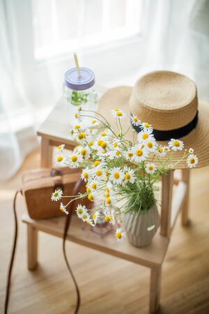 Little wicker women bag, a bouquet of daisies, lemonade with mint, wicker hat, wooden chair. Cozy.の写真素材