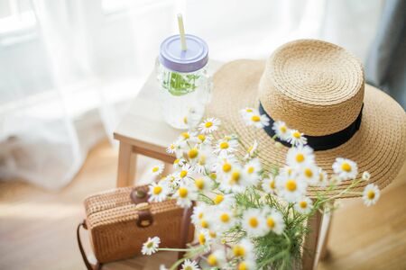 Little wicker women bag, a bouquet of daisies, lemonade with mint, wicker hat, wooden chair. Cozy.の写真素材