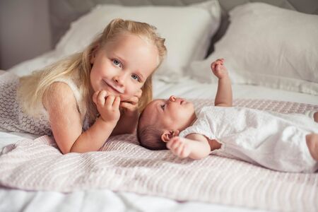 Young beautiful mother holds a baby. Little sister kisses her little sister. Baby. Children bedroom.の写真素材