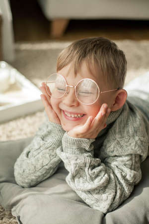 A beautiful little boy in a knitted sweater is reading by the window with a mug of hot tea. Cozy....