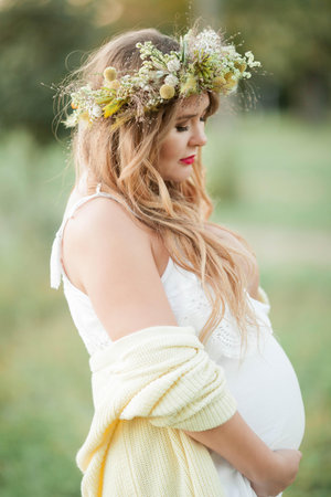 Portrait of a pregnant woman in the sun. Young beautiful pregnant woman with a wreath on her head in the field. Motherhood. Warm autumn. Spring.の写真素材