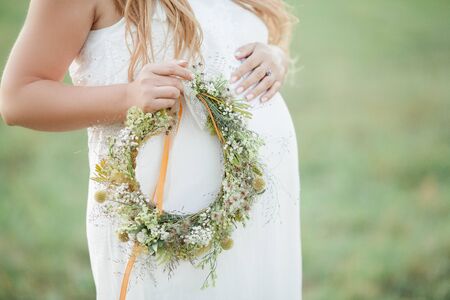 Portrait of a pregnant woman in the sun. Young beautiful pregnant woman with a wreath on her head in the field. Motherhood. Warm autumn. Spring.の写真素材