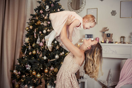 Beautiful and happy young mother holds a little daughter near the Christmas tree. Christmas. New Year. Holidays.の写真素材