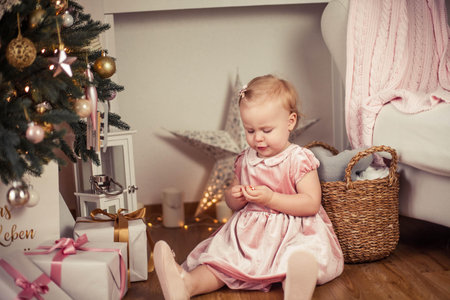 Beautiful little girl with blue eyes in a pink dress holds a gift near the Christmas tree. Christmas. New Year. Holidays.の写真素材