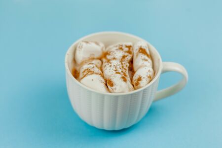 A large white mug with cocoa and marshmallows, cinnamon on a blue background. Christmas motives. Traditional winter drink. Cozy.の写真素材