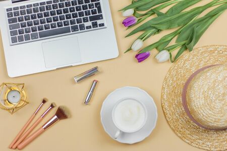 Bouquet of tulips, women's straw hat, laptop, cosmetics, brushes, candle on a beige background. Women's things. Spring.の写真素材