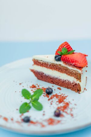 A beautiful piece of cake with berries with butter cream on a blue background. Cake with red cakes. Food.の写真素材