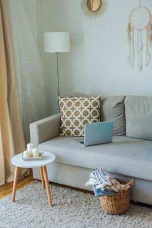 Beautiful stylish interior. The laptop is on the couch, pillow, candles. The cozy corner of the apartment. Spring.の写真素材