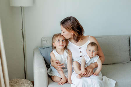 Young happy mother with her daughters in the home interior. Mothers Day. Cozy.