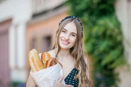 Beautiful young woman in a european city holds a french baguette. French style. City.の写真素材
