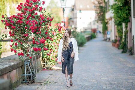 Young beautiful woman walks in a European city. Portrait of a young woman near blooming roses. Europe.の写真素材