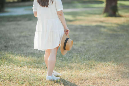 Young woman portrait in sunbeams. A beautiful young woman in a white dress with a wicker straw hat walks in the park.の写真素材