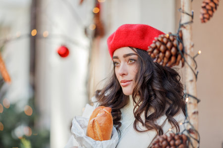 Portrait of a young beautiful woman in a red beret in a European city. Young woman holds a paper bag with baguettes. Christmas. Holidays.の写真素材