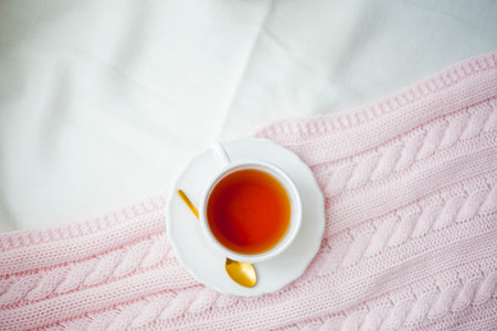 A mug of hot tea, a knitted pink plaid on the bed. Breakfast in bed. Cozy. Spring.の写真素材