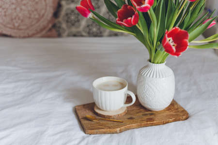 Breakfast in bed. A mug of coffee, a bouquet of tulips in a vase, a wooden tray. Women's Day....