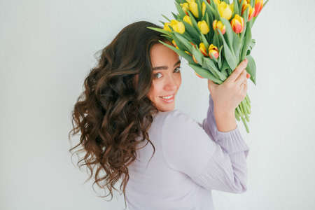 Beautiful young woman with curly hair holds a bouquet of tulips. Women's Day.の写真素材