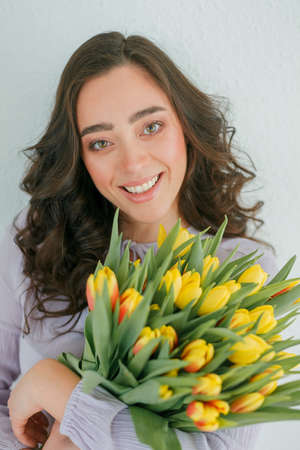 Beautiful young woman with curly hair holds a bouquet of tulips. Women's Day.の写真素材