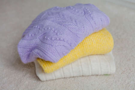 A stack of knitted sweaters. Clothes for spring. Trending colors, yellow, lilac. Cozy.の写真素材