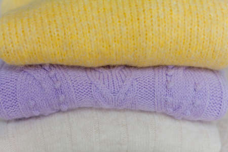 A stack of knitted sweaters. Clothes for spring. Trending colors, yellow, lilac. Cozy.の写真素材